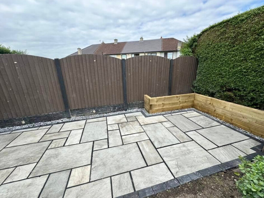 Paved patio with raised timber sleeper planters and dark fencing