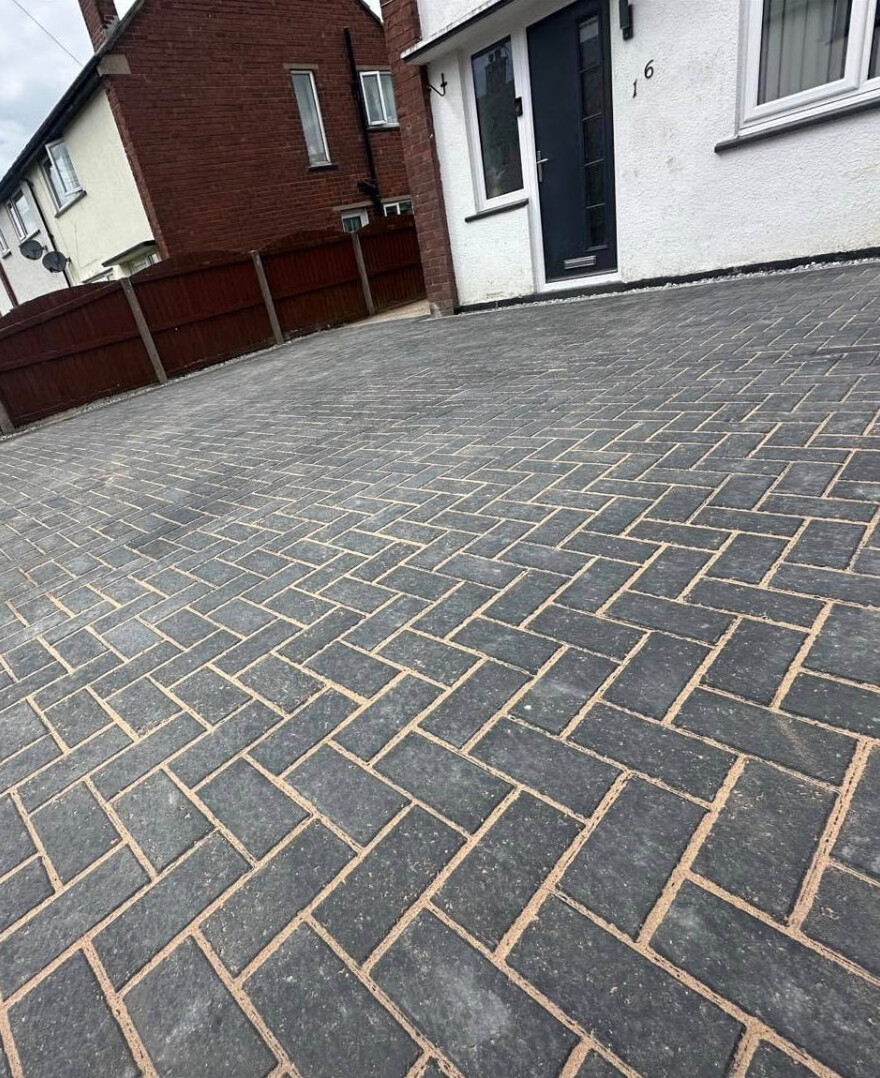 Dark charcoal herringbone block-paved driveway in front of a house